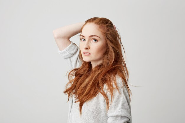 Portrait of young pretty ginger girl with freckles touching hair .