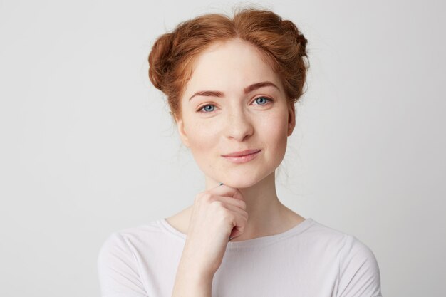 Portrait of young pretty girl with red hair smiling touching chin .