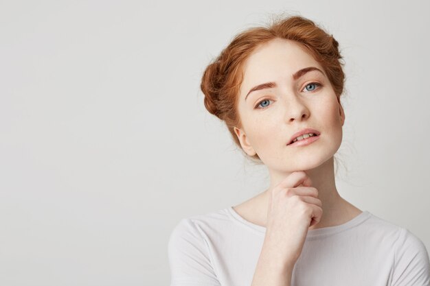 Portrait of young pretty girl with red hair touching chin .