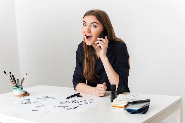 하얀 책상에 앉아 휴대폰 통화를 하는 젊은 미녀 초상화