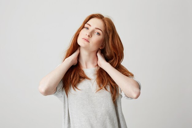 Portrait of young pretty redhead girl touching neck .