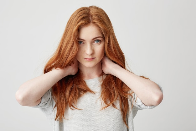 Portrait of young pretty redhead girl touching neck .