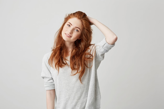 Portrait of young pretty redhead girl with freckles smiling touching hair .