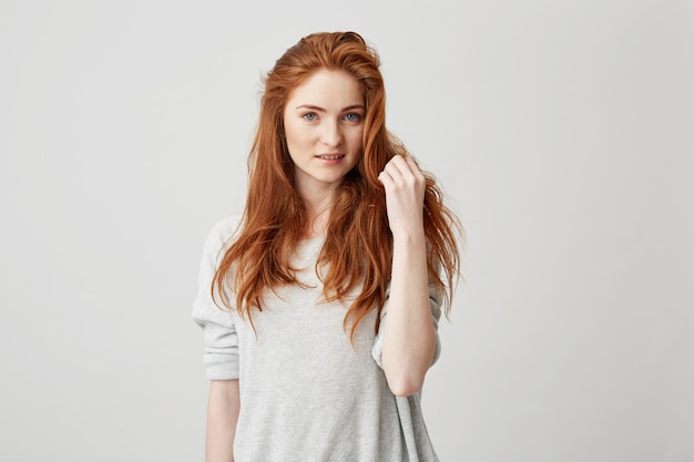 Portrait of young pretty redhead girl with freckles smiling touching hair .