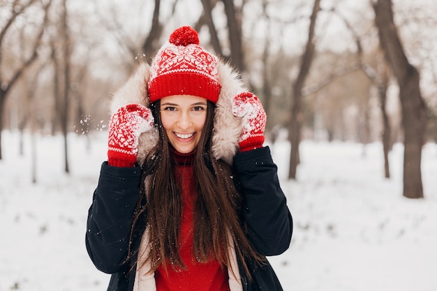 Foto gratuita ritratto di giovane donna felice piuttosto sorridente in guanti rossi e cappello lavorato a maglia che indossa cappotto invernale, passeggiate nel parco nella neve, vestiti caldi