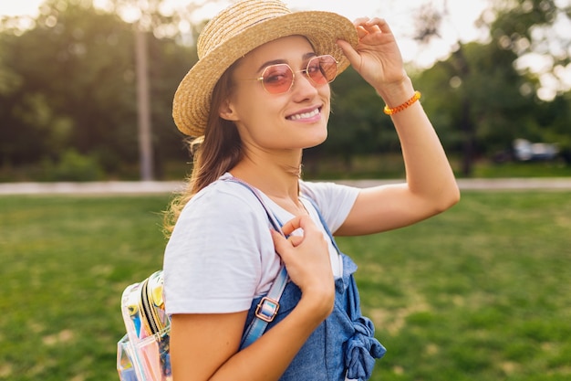 Portrait of young pretty smiling woman in straw hat and pink sunglasses walking in park, summer fashion style, colorful hipster outfit