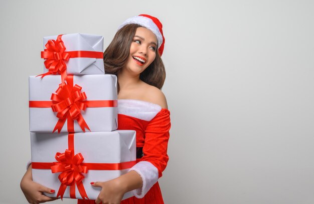Portrait young pretty woman in red santa claus costume, smile and holding gift box in her arms, copy space isolated on gray background
