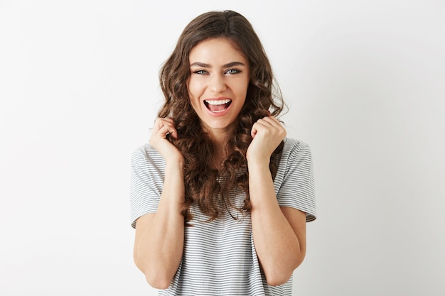 Portrait of young pretty woman in t-shirt laughing, holding hands up, isolated, happy, long curly hair, white teeth