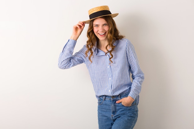 Portrait of young pretty woman with straw hat jeans blue cotton shirt posing on white wall