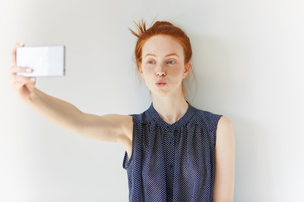 Portrait of young red-haired woman taking selfie