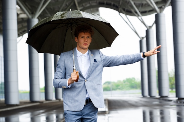 Free photo portrait  of young redhaired businessman catching the car and holding umbrella