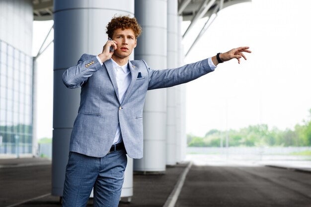 Portrait of young redhaired businessman catching the car and talking on phone