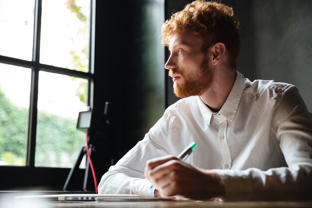 Portrait of a young redhead man writing in a notebook