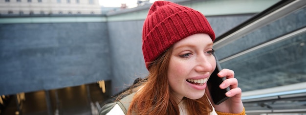 Portrait of young redhead woman walks around city goes up stairs with mobile phone talks on