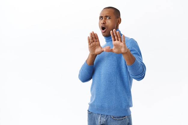 Free photo portrait of young reluctant nervous african-american man telling stay away from me, making block with raised hands, stop gesture