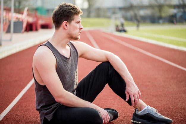 Portrait of young runner sitting on race track