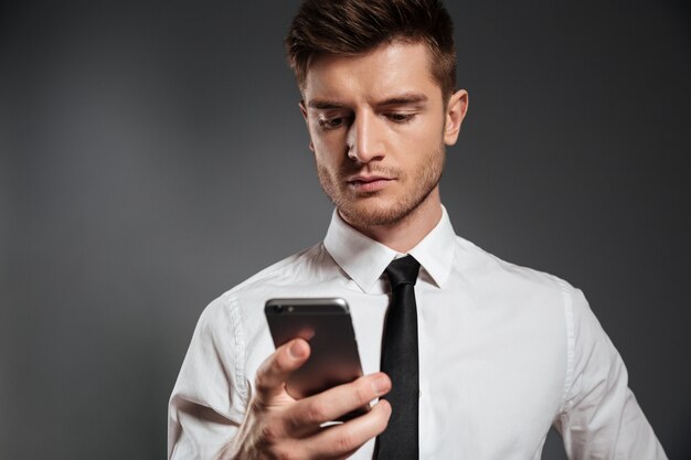 Портрет молодого серьезного бизнесмена используя мобильный телефон