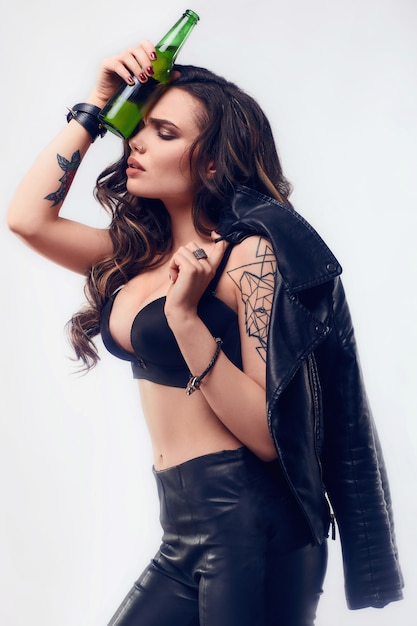 Портрет молодой сексуальной женщины с длинными волосами в кожаной куртке, держащей бутылку пива
