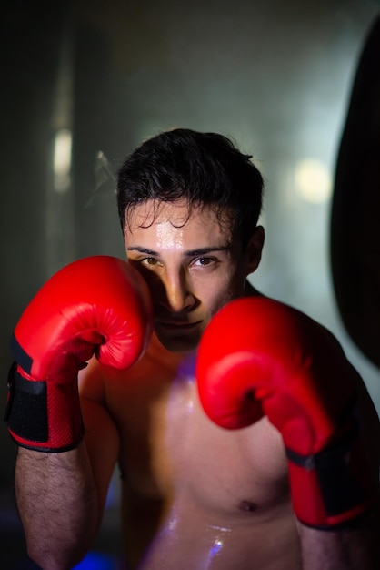 Portrait of young shirtless boxer in red gloves. Dedicated multiethnic man standing in fighting pose. Sportsman concept
