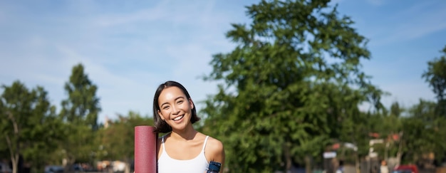 Free Photo portrait of young slim and healthy korean girl doing workout in park standing with water bottle and