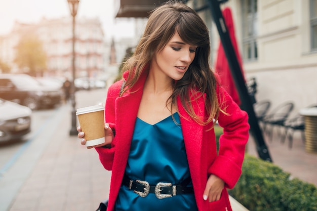 커피를 마시는 빨간 코트에 도시 거리에서 걷는 젊은 미소 아름 다운 세련 된 여자의 초상화