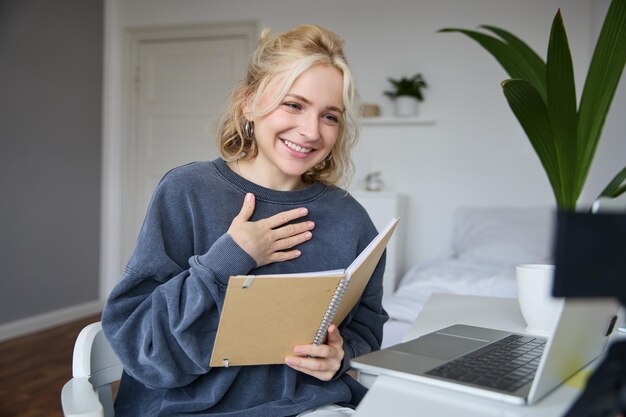 Portrait of young smiling blond woman working from home online chatting using digital video camera