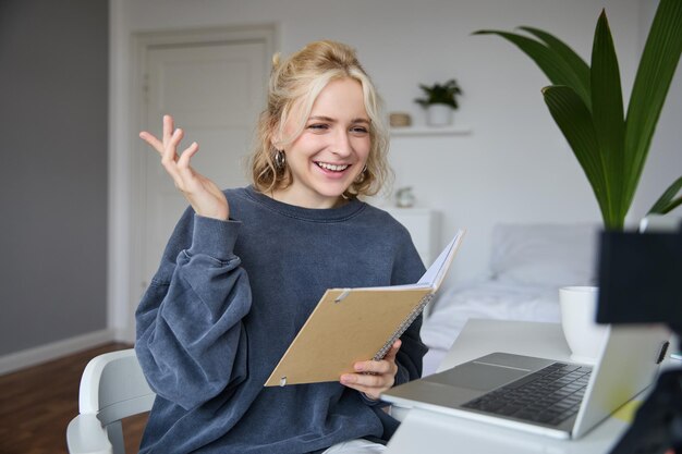 Portrait of young smiling blond woman working from home online chatting using digital video camera