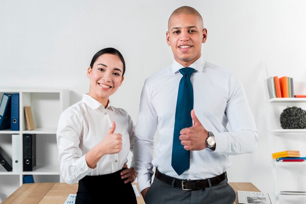 Portrait of a young smiling businessman and businesswoman showing thumb up sign