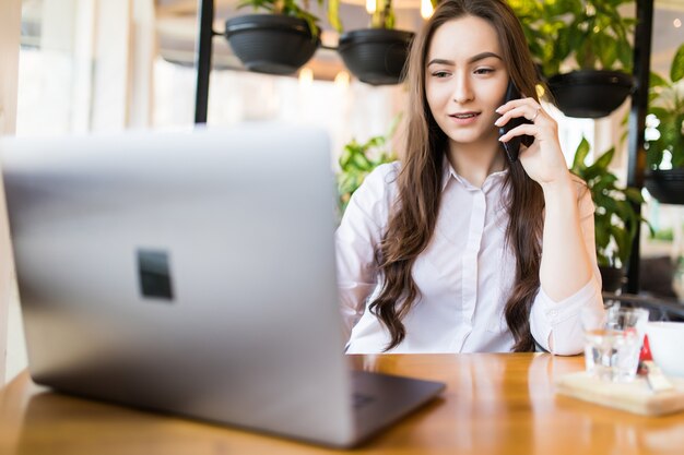 Portrait of young smiling businesswoman calling her best friend, having break, telling something funny, sitting in cafe