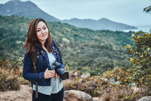 Portrait of a young smiling chinese woman with photo camera in hands. She enjoy beautiful sights of nature.