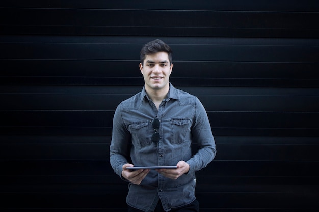 Portrait of young smiling handsome man holding tablet computer and looking straight to the front