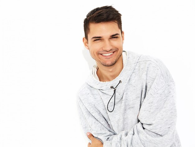 Portrait of young smiling handsome model man dressed in gray casual hoodie clothes posing on white wall. Isolated