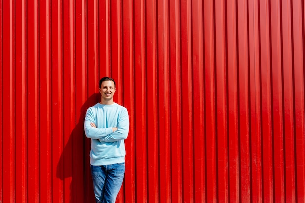 Portrait of young smiling man in blue jacket on the background of red wall