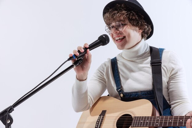 Portrait of young smiling man singing and playing guitar isolated over white studio background