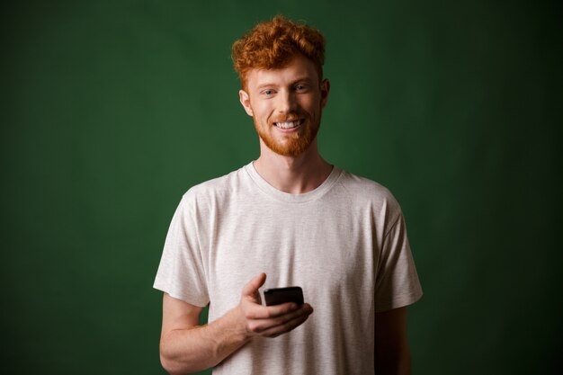 Portrait of young smiling redhead bearded young man, holding mobile phone