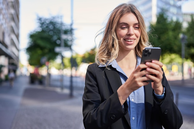 Foto gratuita ritratto di giovane donna d'affari sorridente commessa guardando il suo telefono cellulare con faccia felice rea