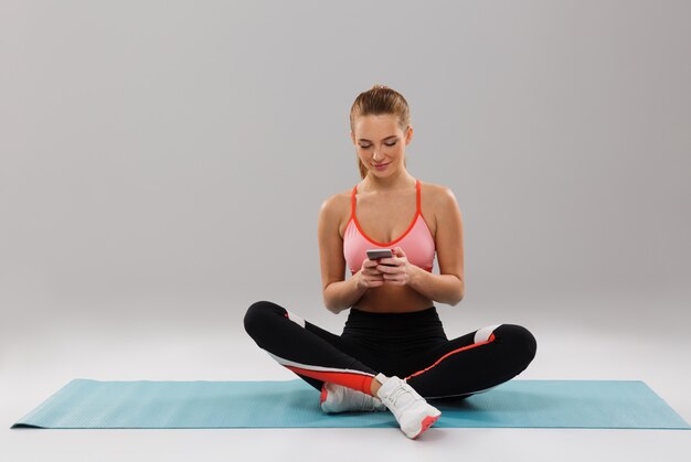 Portrait of a young smiling sportsgirl using mobile phone