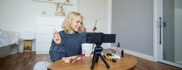 Free photo portrait of young smiling woman in her room recording video on camera lifestyle vlog for social