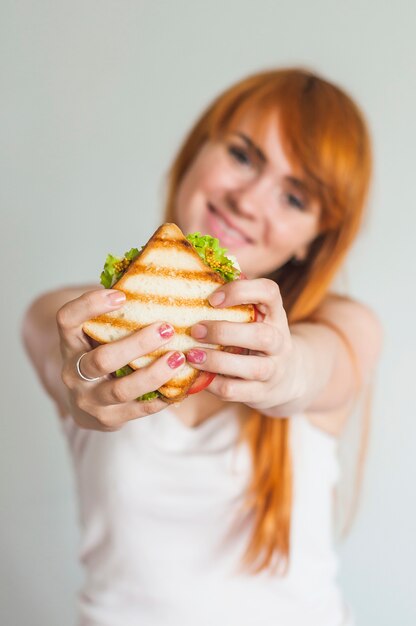 Portrait of young smiling woman showing grilled sandwich against white background