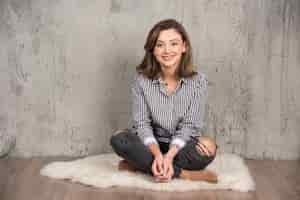 Free photo portrait of a young smiling woman sitting on the floor and posing.