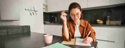 Free photo portrait of young smiling woman tutor preparing notes for lesson at home writing in notebook and