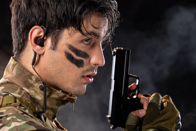 Portrait of young soldier in camouflage aiming gun on black wall