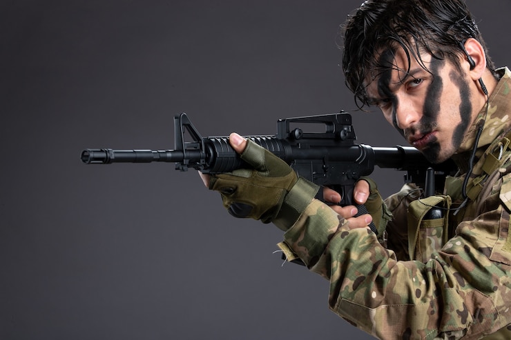 Portrait of young soldier in camouflage aiming machine gun on dark wall