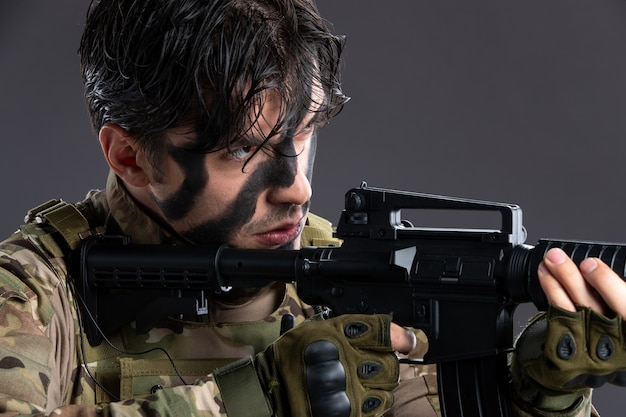 Ritratto di giovane soldato in mimetica che mira mitragliatrice sulla parete scura