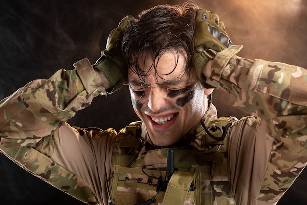 Portrait of young soldier in camouflage having headache on black wall