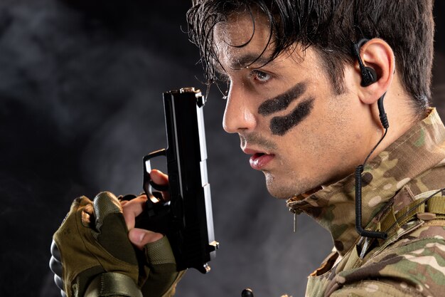 Portrait of young soldier in camouflage holding gun on black wall