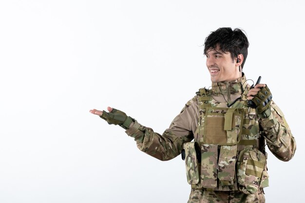 Portrait of young soldier in camouflage talking through walkie-talkie light wall