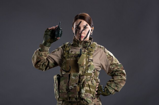 Portrait of young soldier in camouflage with grenade on dark wall