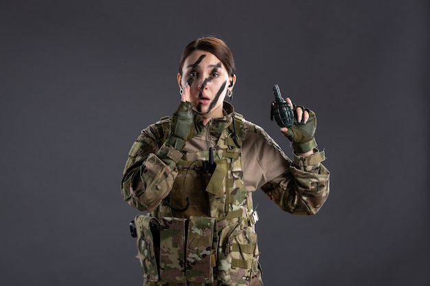 Portrait of young soldier in camouflage with grenade on her hands dark wall
