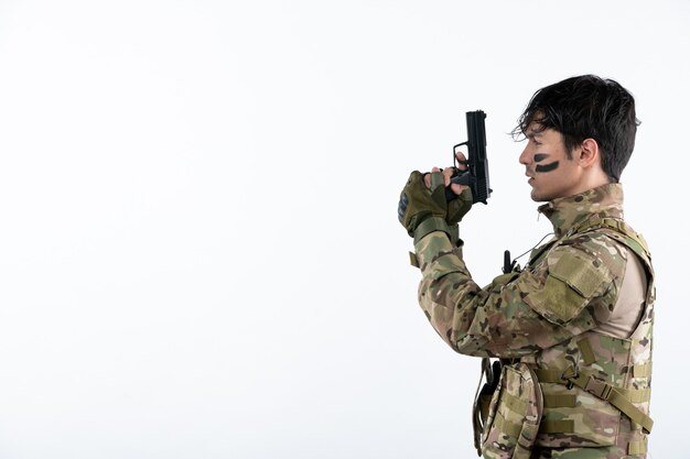 Портрет молодого солдата в камуфляже с пушкой студия выстрелил в белую стену
